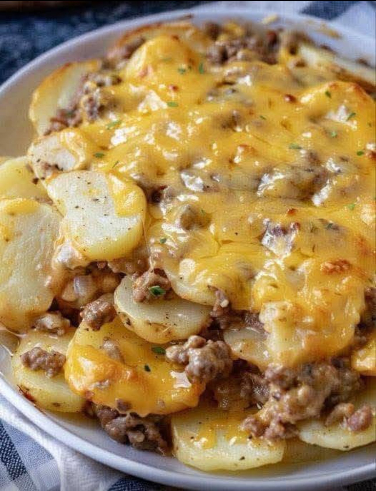 A baked cheesy ground beef casserole with golden brown melted cheddar, sliced potatoes,