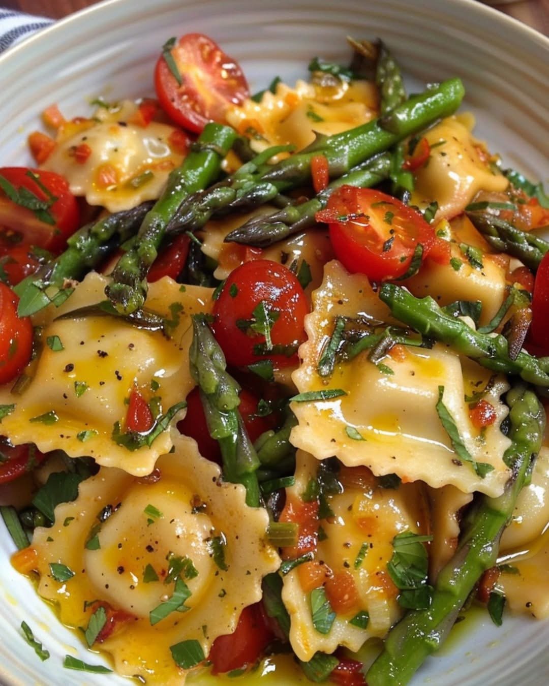 Ravioli pasta with asparagus, cherry tomatoes, garlic, and fresh herbs on a white plate
