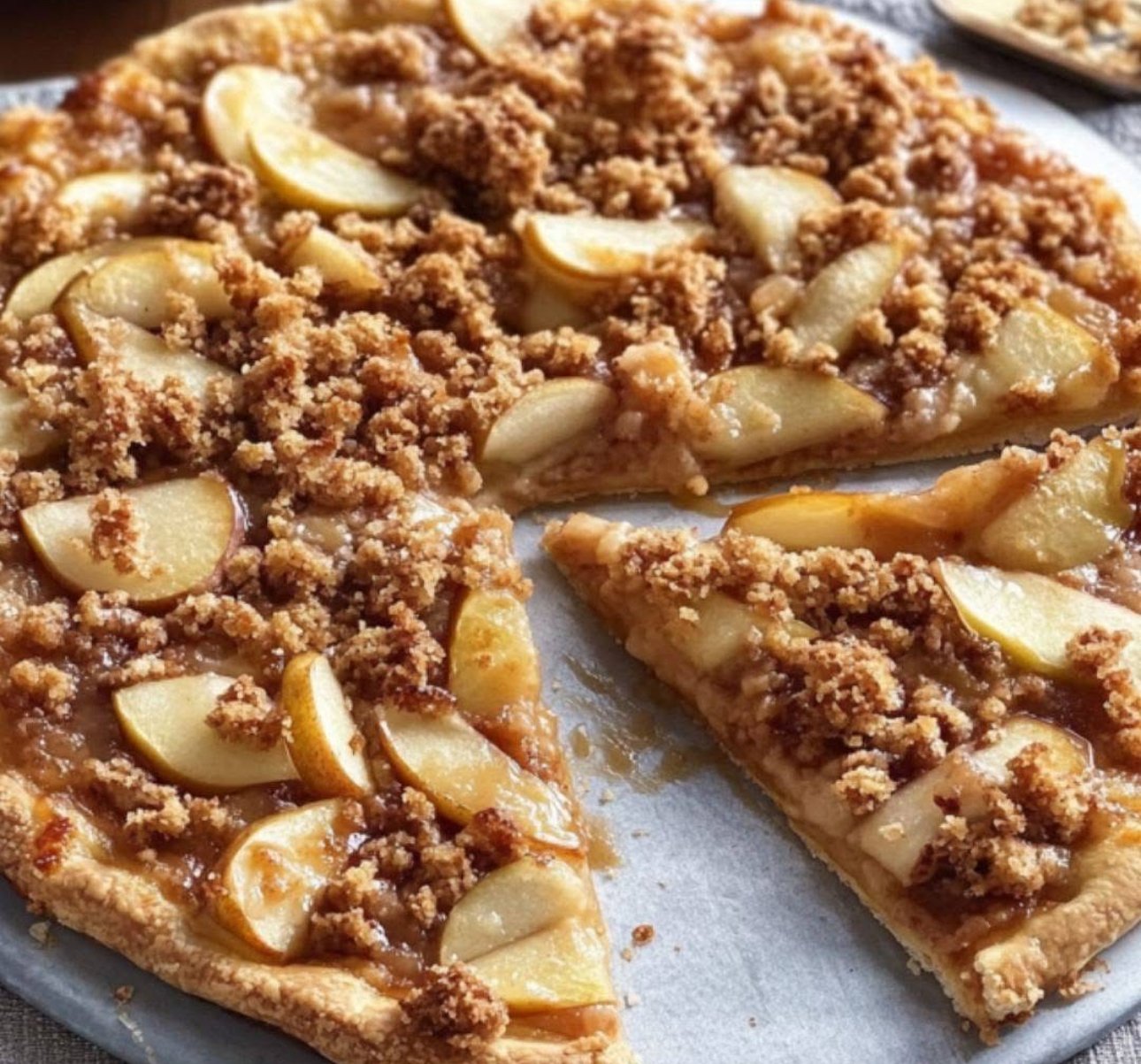 Golden apple crisp pizza topped with oats, cinnamon crumble, and caramel drizzle, served warm with vanilla ice cream.