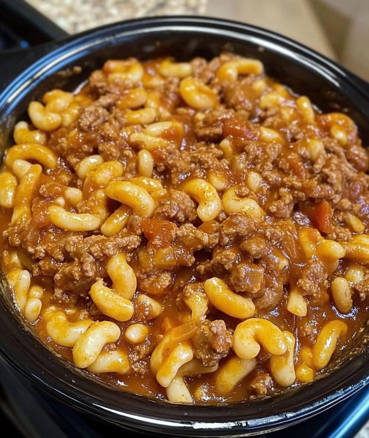 Ground beef, onions, bell peppers, garlic, and pasta on a countertop for Crockpot goulash