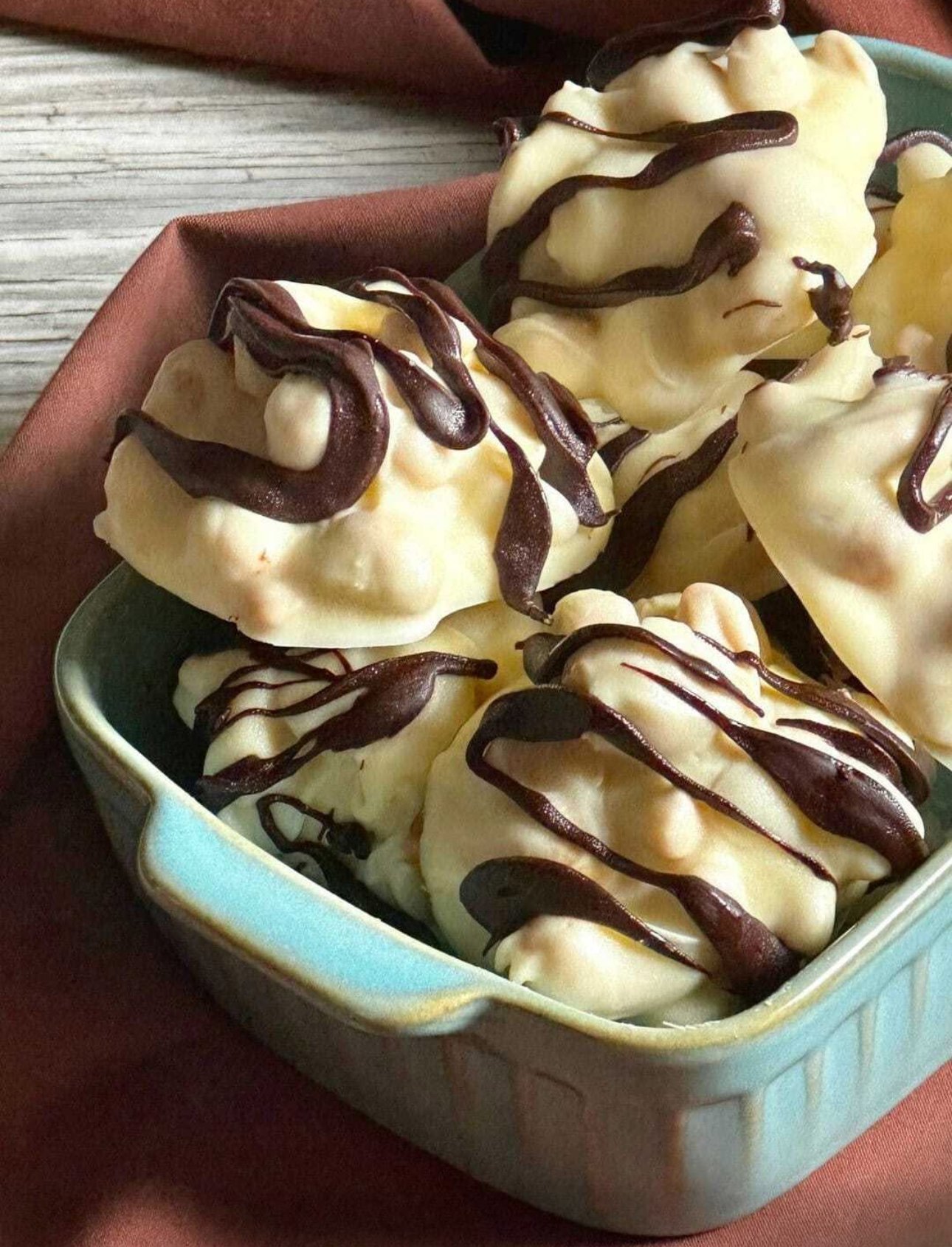 Milk chocolate drizzle over cashew clusters on baking sheet.
