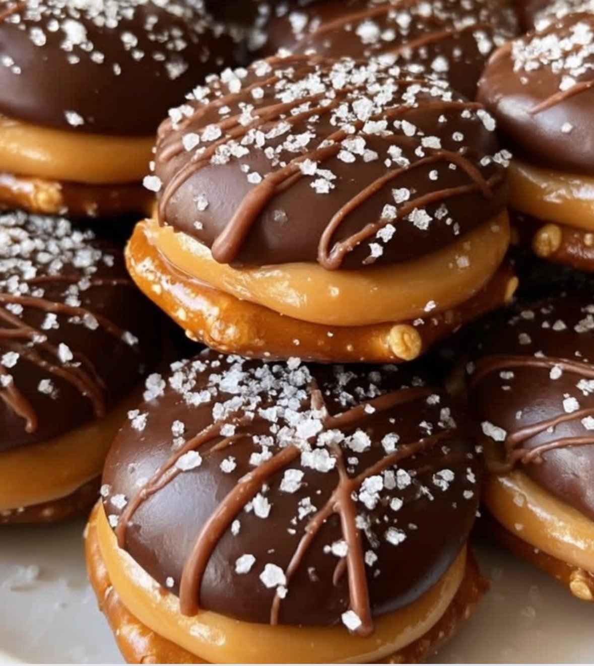 No-bake salted caramel pretzel bites with chocolate drizzle and sea salt on parchment paper.