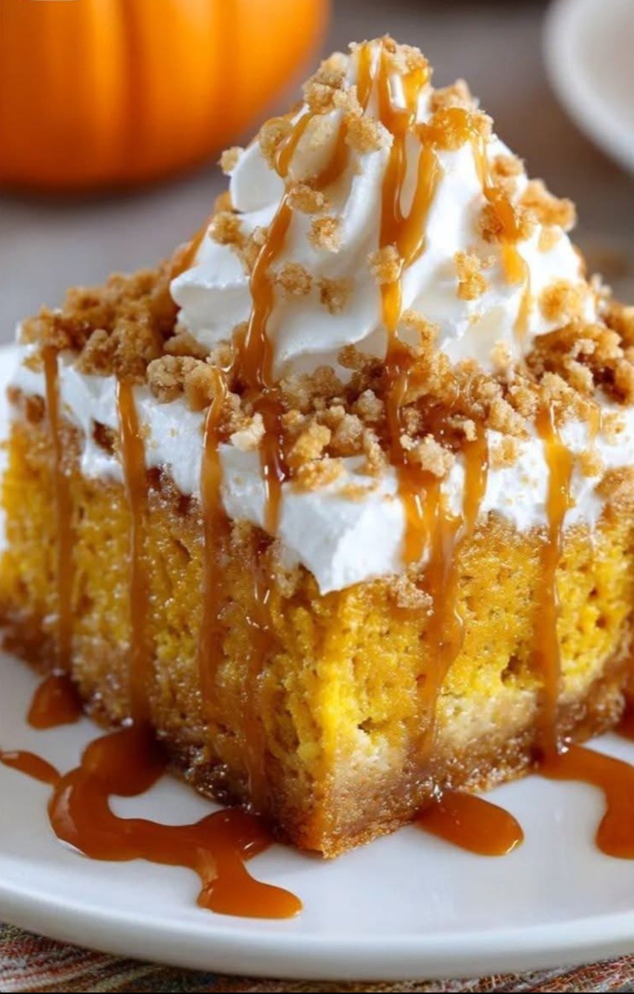 Layered pumpkin spice gooey cake with brown sugar cream cheese frosting, garnished with caramel drizzle and spiced pecans