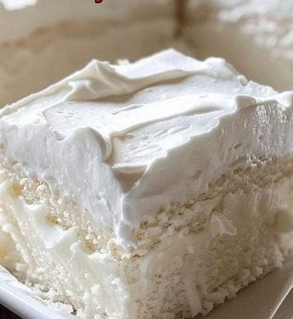 Fluffy homemade Heavenly White Snack Cake baked in an 8x8 pan, topped with light frosting and sliced into squares.