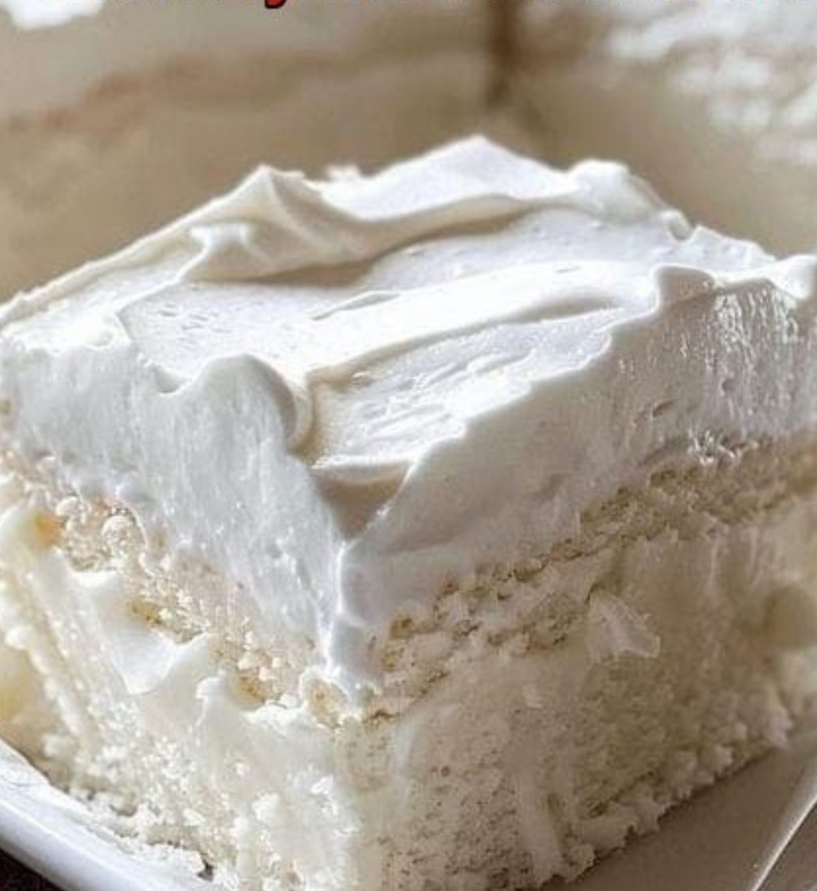 Fluffy homemade Heavenly White Snack Cake baked in an 8x8 pan, topped with light frosting and sliced into squares.