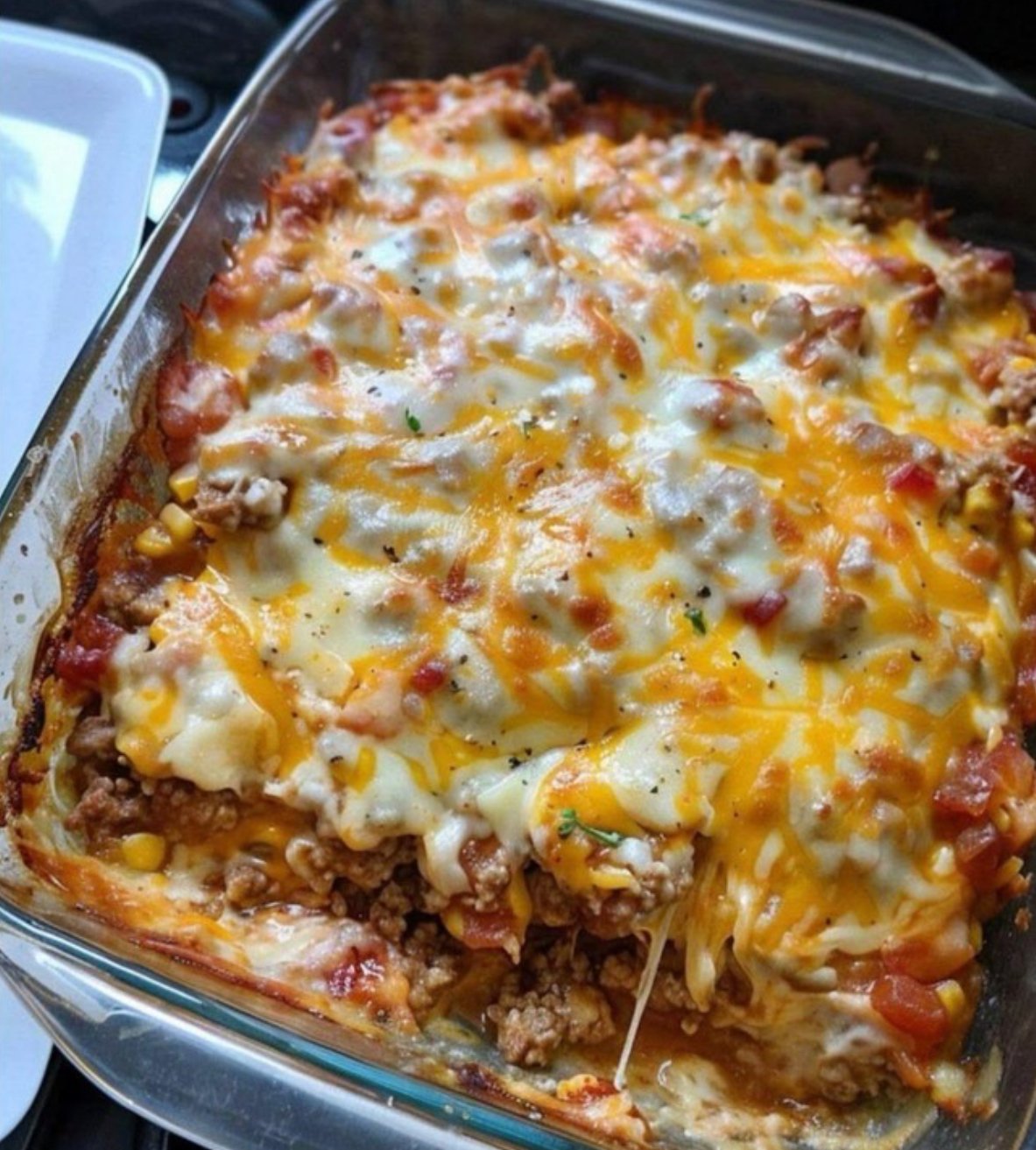 Homemade creamy beef and noodle casserole with layers of seasoned ground beef, tomato sauce, sour cream, and melted cheddar cheese baked in a 9x13 casserole dish.