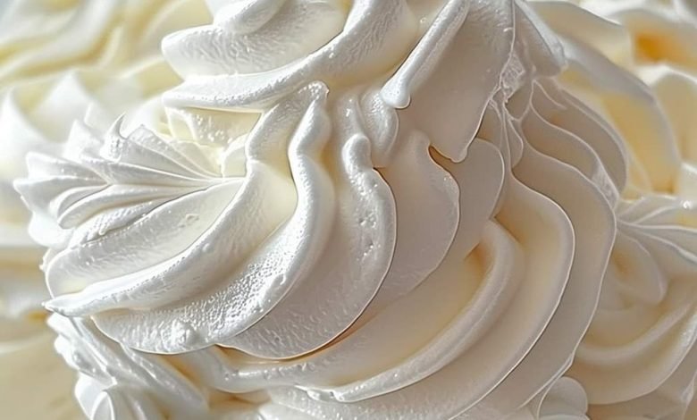 A bowl of glossy 7-Minute Frosting with peaks, ready to spread on a cake, made from sugar, egg whites, and vanilla extract.