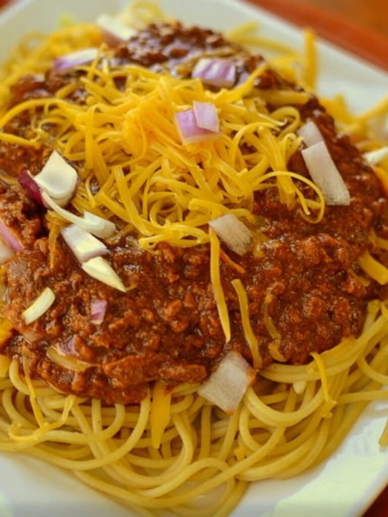 Bowl of Cincinnati chili over spaghetti noodles, topped with cheddar cheese and onions.