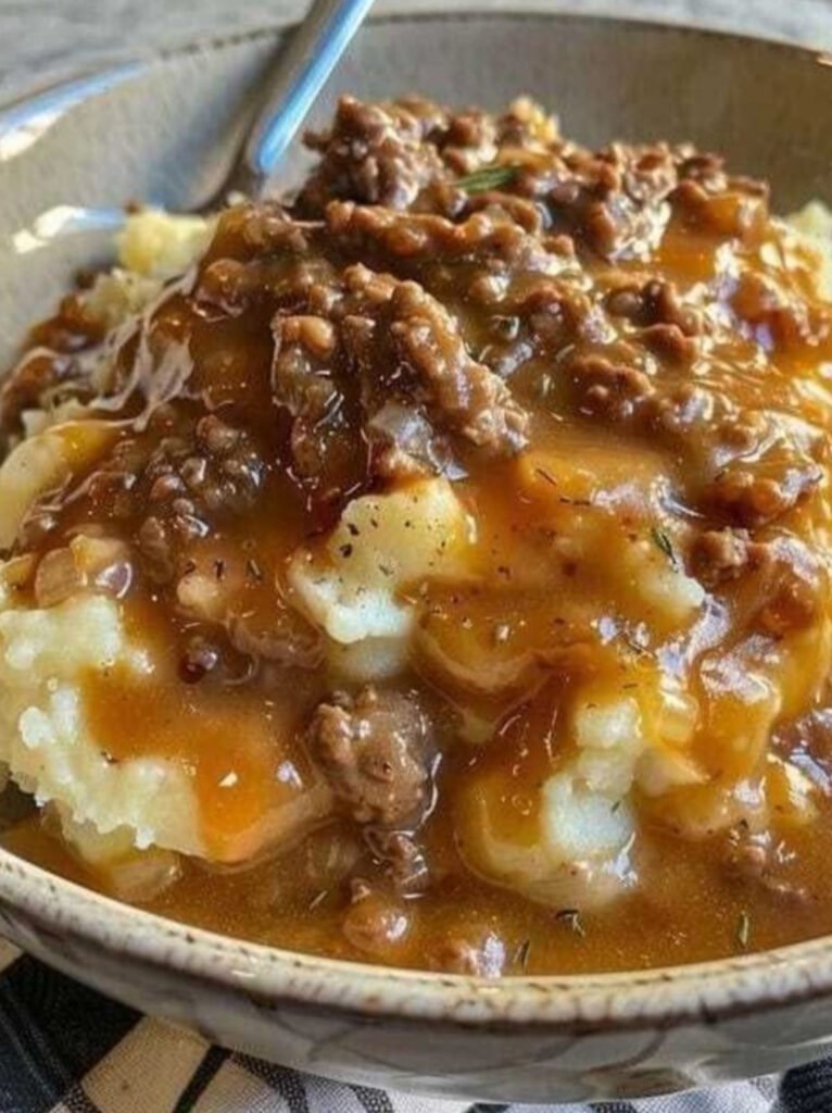 Plate of mashed potatoes with thick ground beef gravy and carrots and peas.