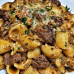 Garlic butter steak bites served over creamy Parmesan pasta shells with parsley garnish