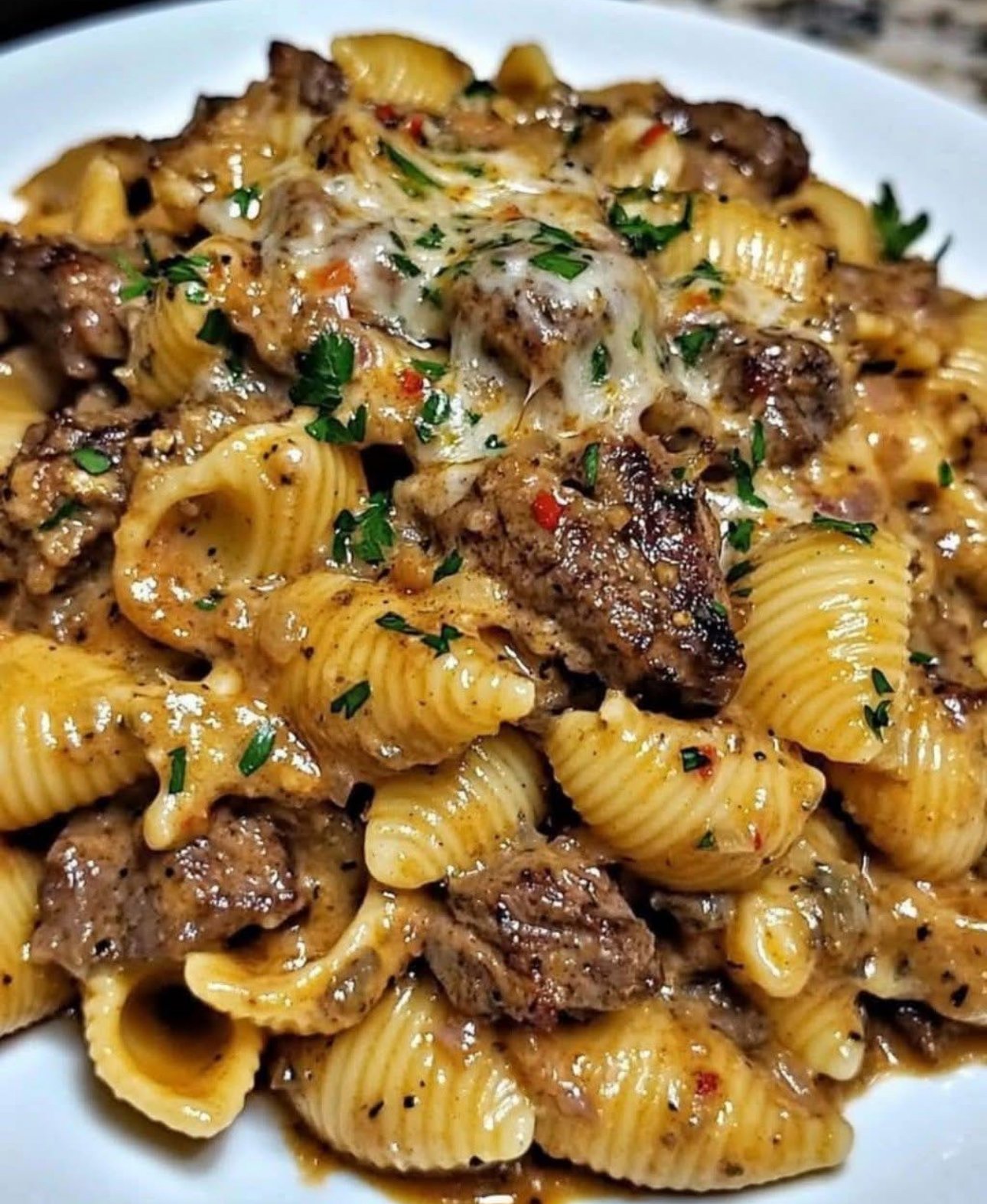 Garlic butter steak bites served over creamy Parmesan pasta shells with parsley garnish
