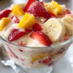Creamy fruit salad made with strawberries, bananas, and yogurt served in a glass bowl