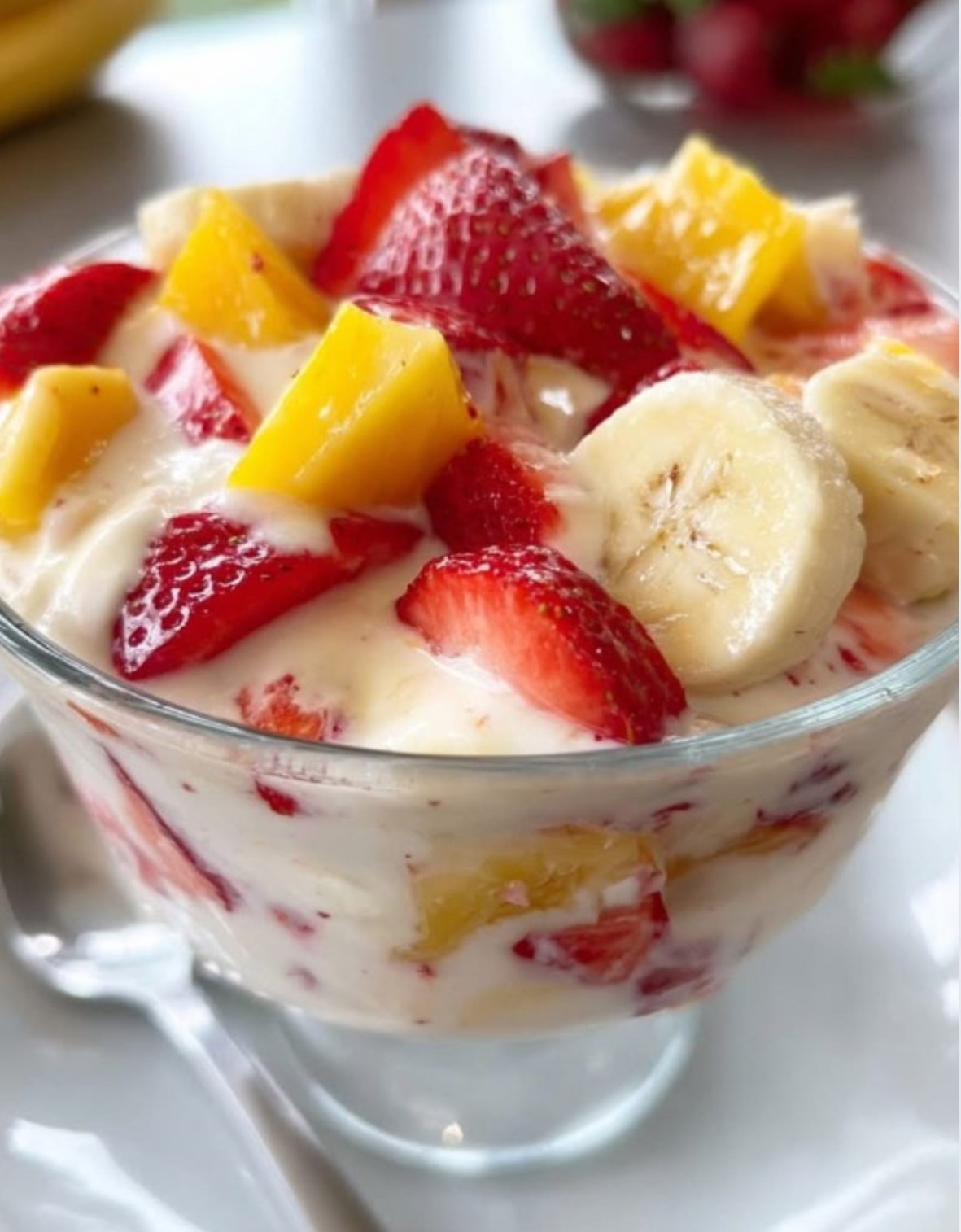 Creamy fruit salad made with strawberries, bananas, and yogurt served in a glass bowl